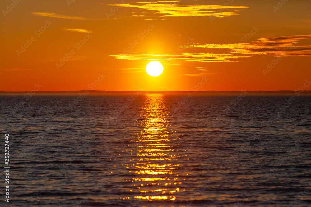 bright orange sun with reflection in the water during sunset over the sea