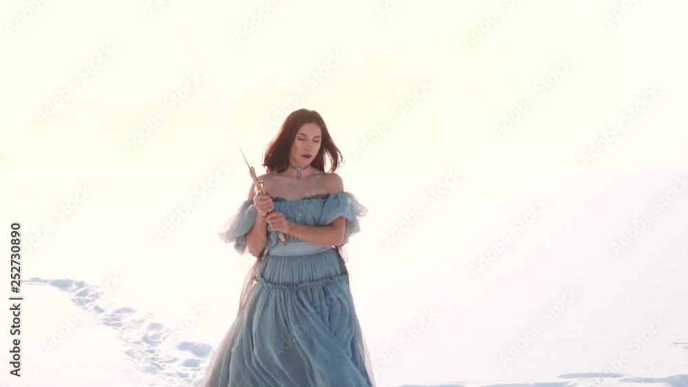 girl with dark hair and stern look bravely and confidently walks through snow to enemy, lady in a long gray vintage light dress with open shoulders and sword in hands, ruthless goddess of war girl with dark hair and stern look bravely and confidently walks through snow to enemy, lady in a long gray vintage light dress with open shoulders and sword in hands, ruthless goddess of war