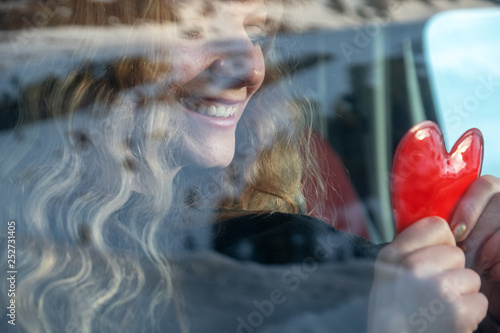 junge sexy Frau mit blonden lockigen Haaren sitzt im Winter im Auto und wärmt sich glüclich an einem Handwärmer als Herz die Hände. photo