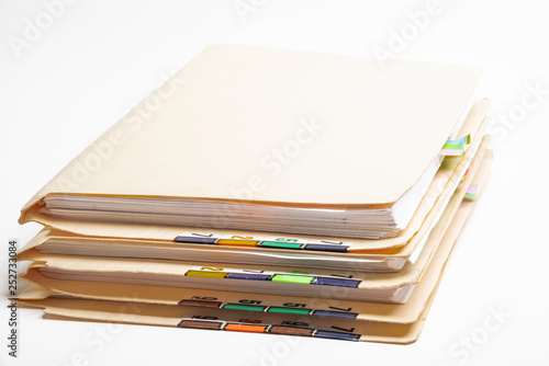 A stack of color-coded and numbered yellow file folders containing sheets of papers, files and documents set on a white background. photo