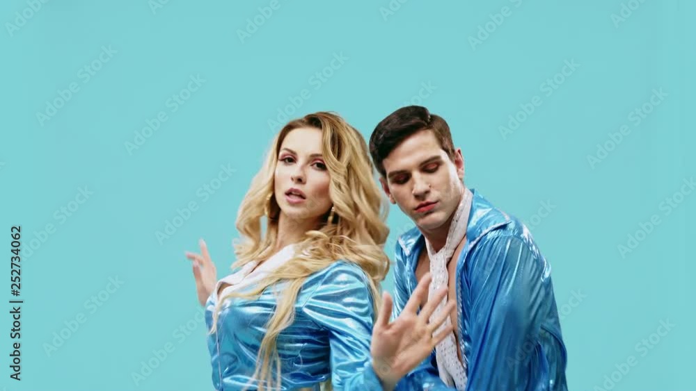 Loving young couple dressed in stylish matching blue outfits dancing close together gesturing with their hands over a blue studio background. Loving young couple dressed in stylish matching blue outfits dancing close together gesturing with their hands over a blue studio background.