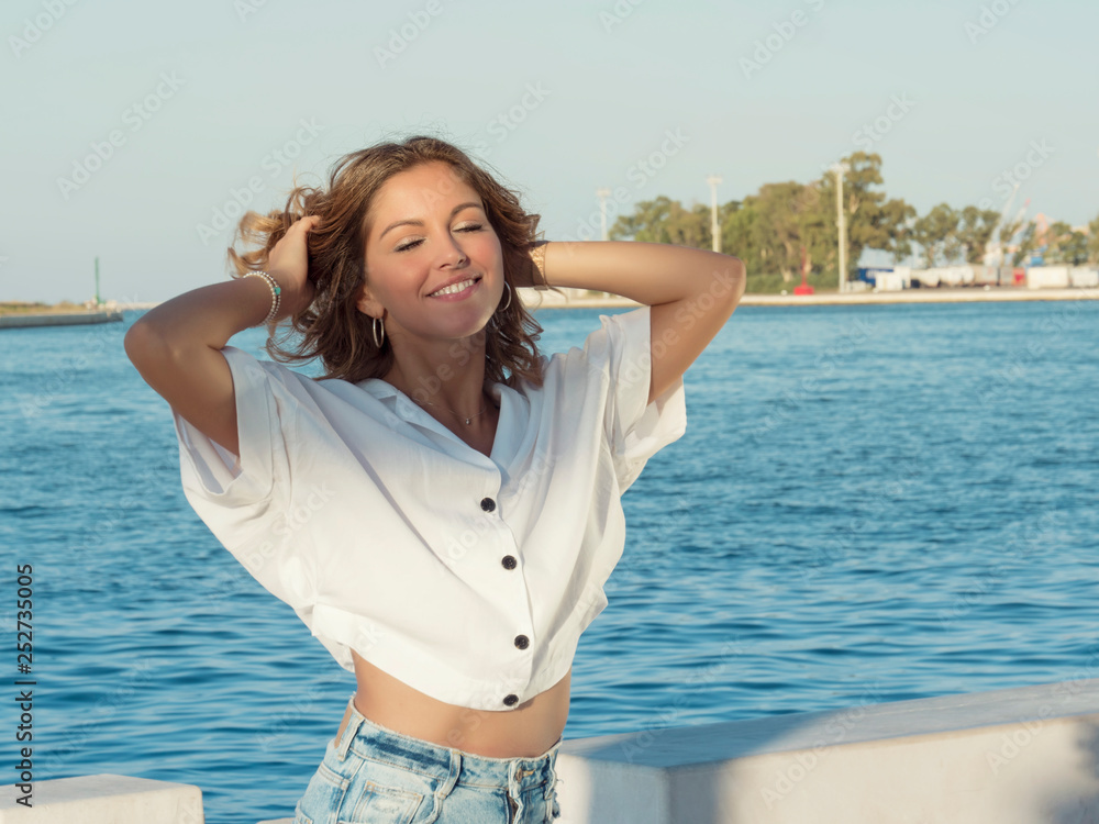 portrait of attractive smile teenage girl with hands behind head, neck, in white shirt, with blonde hair portrait of attractive smile teenage girl with hands behind head, neck, in white shirt, with blonde hair