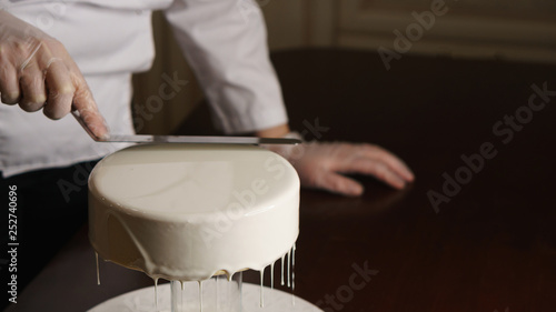 Confectioner fills cakes with white liquid glaze. She equals top surface of cake.