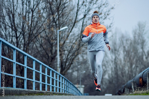Full length of athletic woman running on a bridge during cold weather.