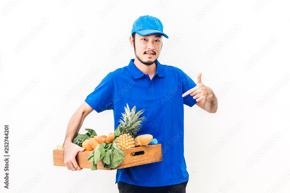 Happy delivery man in blue uniform carrying package of grocery food with vegetable and fruit on white background Happy delivery man in blue uniform carrying package of grocery food with vegetable and fruit on white background