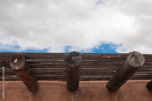 Exterior red adobe building with beams and wood sun screen slats, blue sky and clouds, horizontal aspect photo