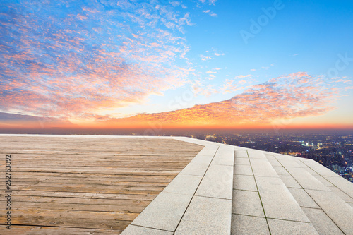Empty wooden platform and modern city skyline with beautiful colorful clouds at sunset © ABCDstock