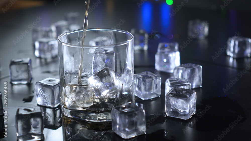 Pouring alcoholic beverages in glass with ice cubes.