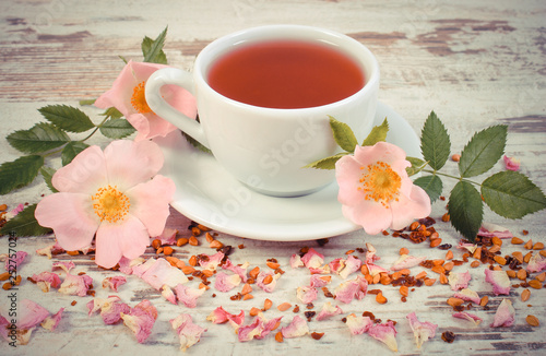 Cup of tea with wild rose flower on old rustic plank