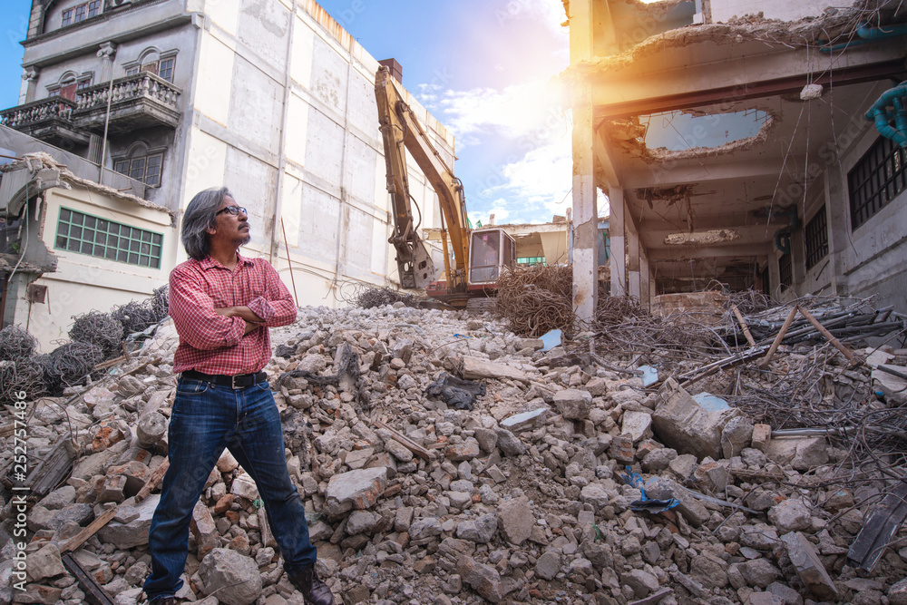 Demolition control supervisor or engineer crossed arms on the pile of bricks over large jackhammer vehicle machine