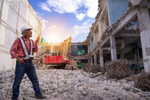 Demolition control supervisor or engineer, taking walkie-talkie in hand over large jackhammer construction vehicle machine