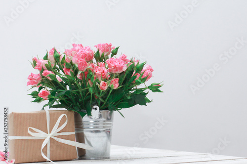 Fototapeta Naklejka Na Ścianę i Meble -  Bunch of roses in tin bucket, petals and gift box on white wooden table. Women day concept. White ribbon, craft wrap, vintage, 8 march, wedding, spring