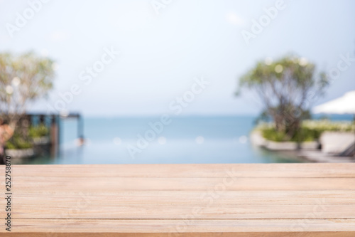 Empty  wood table with blur  a luxury infinity swimming pool in the beach hotel.