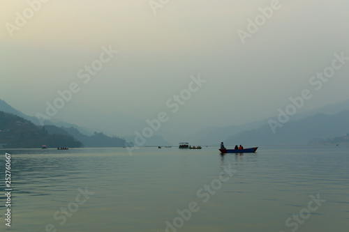 Soft image of relaxing tourists in boats on Lake Fewa in Pokhara, Nepal at sunset. Heavy smog and fog produce persistent grey conditions, creating beautiful and mysterious scenery.