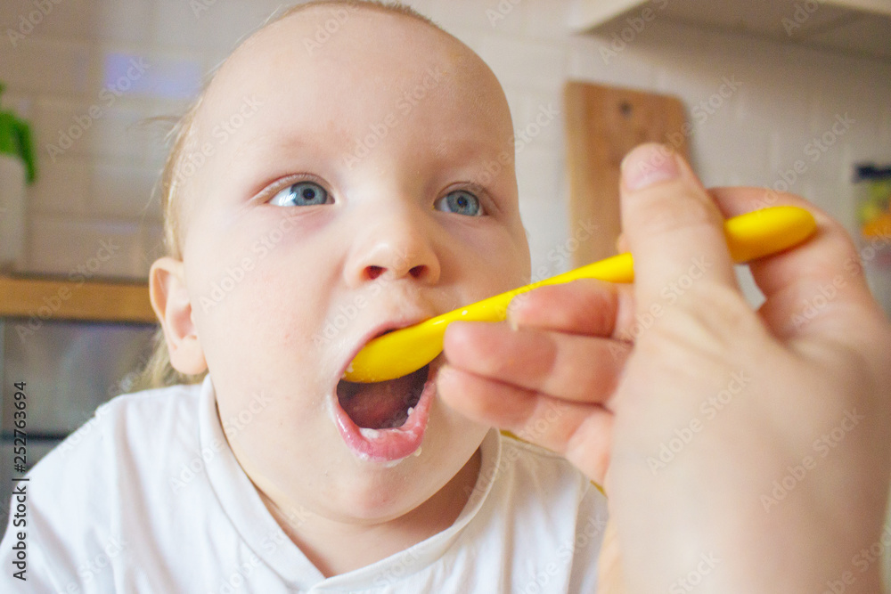 Mother feeds her little son porridge from a yellow spoon Mother feeds her little son porridge from a yellow spoon