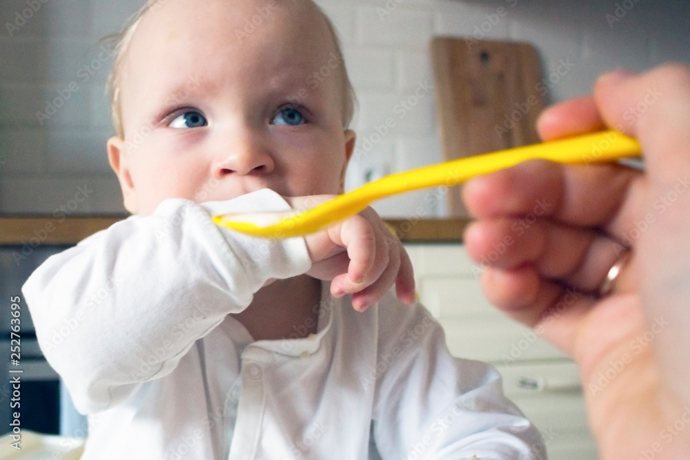 Mother feeds her little son porridge from a yellow spoon Mother feeds her little son porridge from a yellow spoon