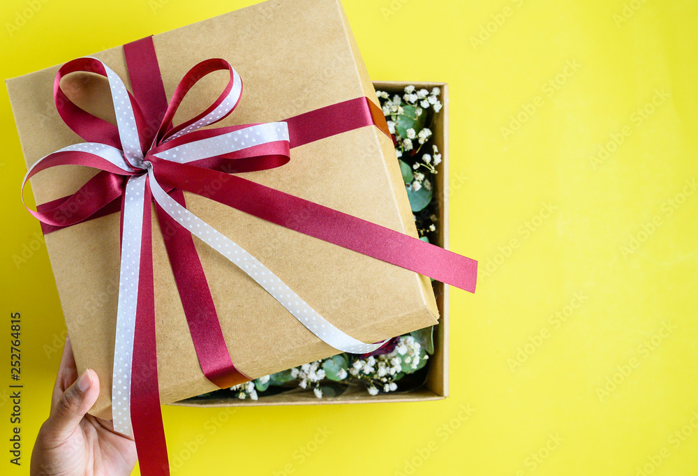 Fototapeta premium Hand open gift box with bow on yellow background