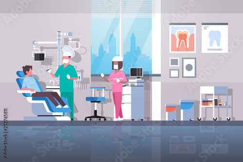 dentist with assistant drilling teeth of man patient lying in dentistry chair professional dental office modern clinic interior mix race characters full length flat horizontal