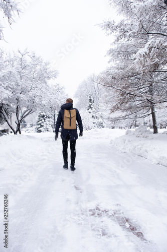 Young businessman walking with a backpack in a snowy park