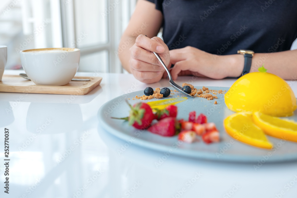 A woman eating orange cake with mixed fruit by spoon in cafe