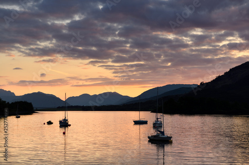 Moored sailboats on Loch Leven with red sky sunset clouds at Glencoe Boat Club and distant Sgurr Dhomhnuill peaks Scottish Highlands Scotland