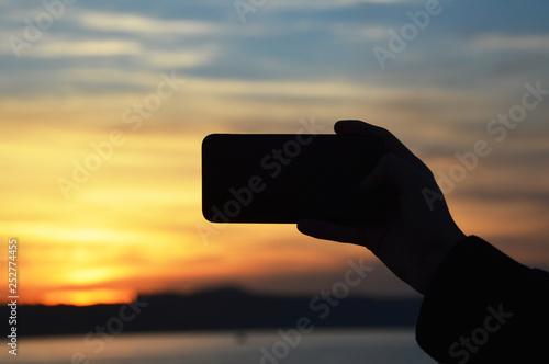 Male hand holding smart phone at the sunset