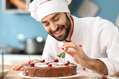 Male confectioner decorating tasty chocolate cake in kitchen photo
