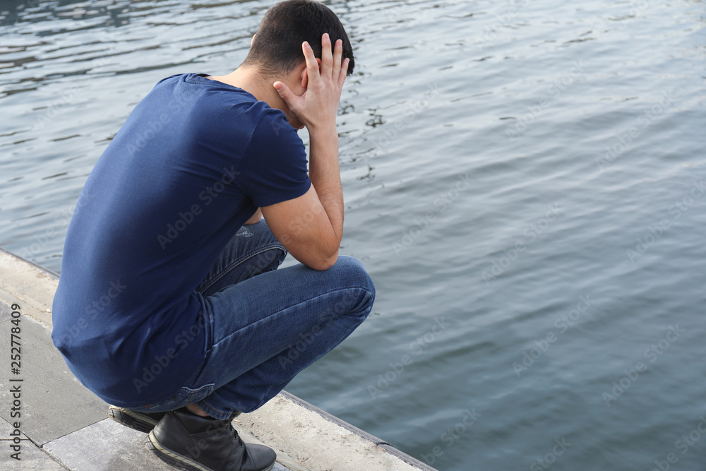Depressed man thinking about suicide on river bank