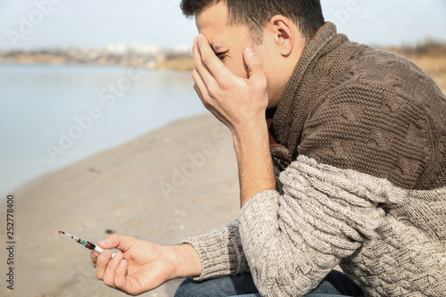 Depressed man with syringe near river. Suicide awareness concept
