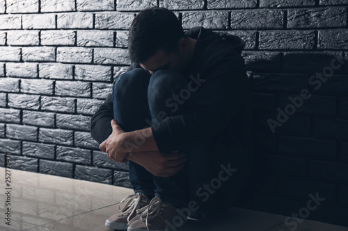 Depressed man thinking about suicide while sitting near dark brick wall