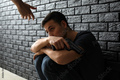 Woman giving hand to depressed man with gun near dark wall. Suicide prevention concept photo