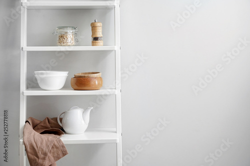 Shelves with kitchenware near white wall