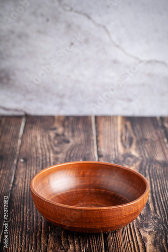 An empty plate of red clay stands on a wooden table, copy space