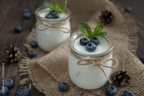 Fresh natural homemade organic yogurt with blueberries, in a glass jar on a wooden background