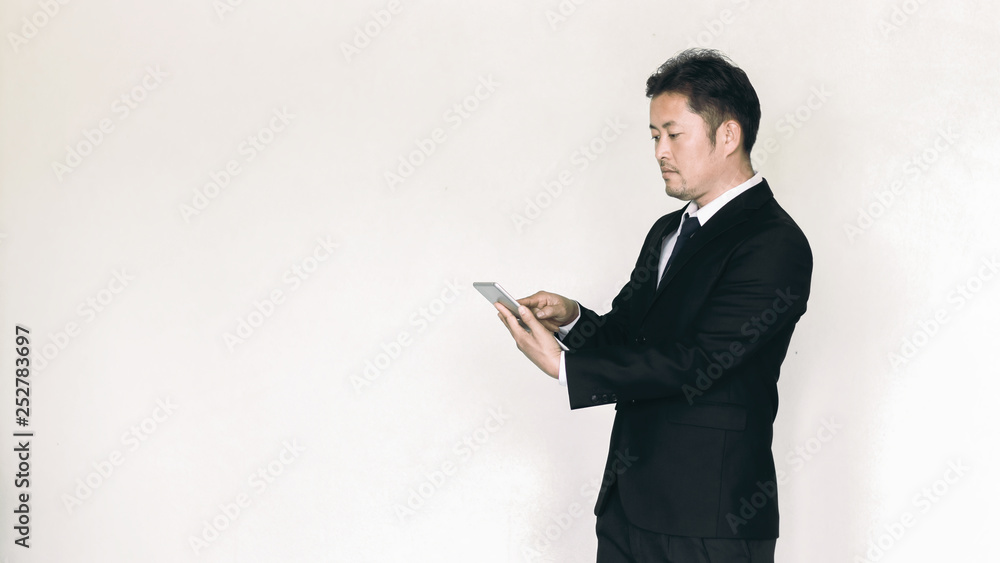 Handsome young asian man holding smart phone and looking at it while standing against grey background Handsome young asian man holding smart phone and looking at it while standing against grey background
