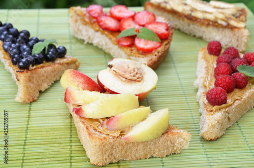 different delicious toasts on green or pink crimson background. Healthy sandwich for breakfast or snack. Toast with raspberries, strawberries, banana and blueberries and peanut butter. picnic concept