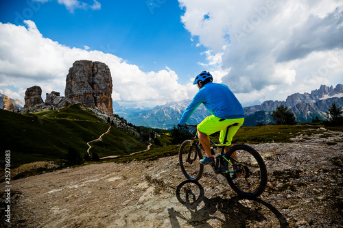 Tourist cycling in Cortina d'Ampezzo, stunning Cinque Torri and Tofana in background. Man riding MTB enduro flow trail. South Tyrol province of Italy, Dolomites.