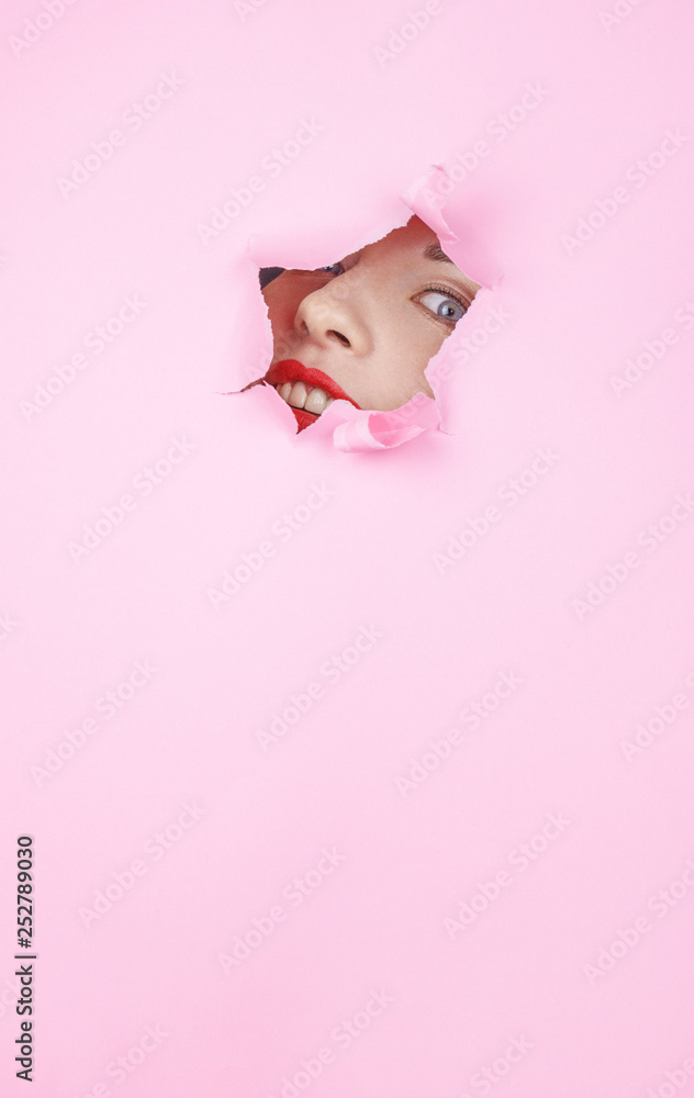Fashion close up minimalistic portrait. Woman face with red lips and perfect skin in pink paper hole background