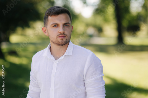 Handsome man in a white shirt and shorts smile. Male model outside. Background of park. Young attractive man walking in the park