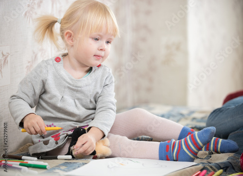 A little blonde baby girl in bright socks sitting on the bed