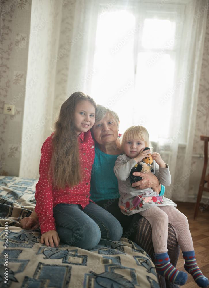 Happy family sitting on the bed. Two girls and grandmother Happy family sitting on the bed. Two girls and grandmother