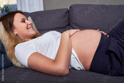Happy pregnant woman smiling stroking belly lying on sofa