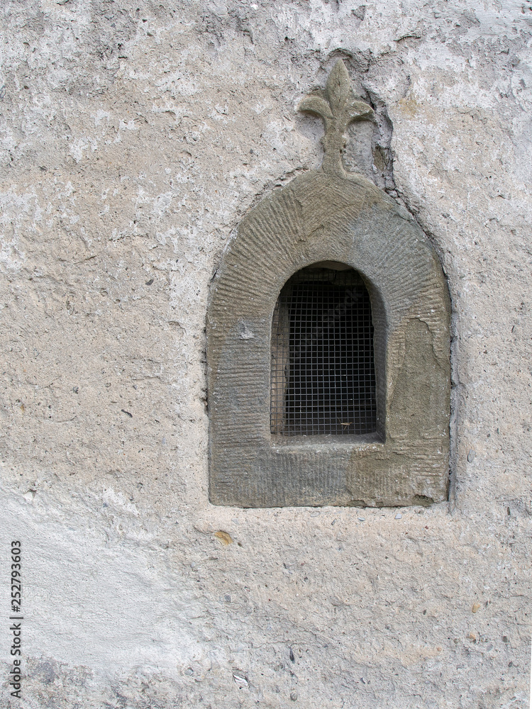 Old stone window with fleur de lys religious motif and grille.