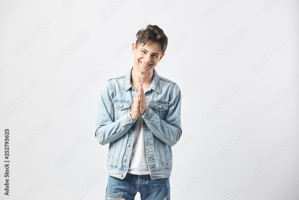 Friendly dark-haired guy dressed in a white t-shirt, jeans and a denim jacket stands on the white background in the studio Friendly dark-haired guy dressed in a white t-shirt, jeans and a denim jacket stands on the white background in the studio