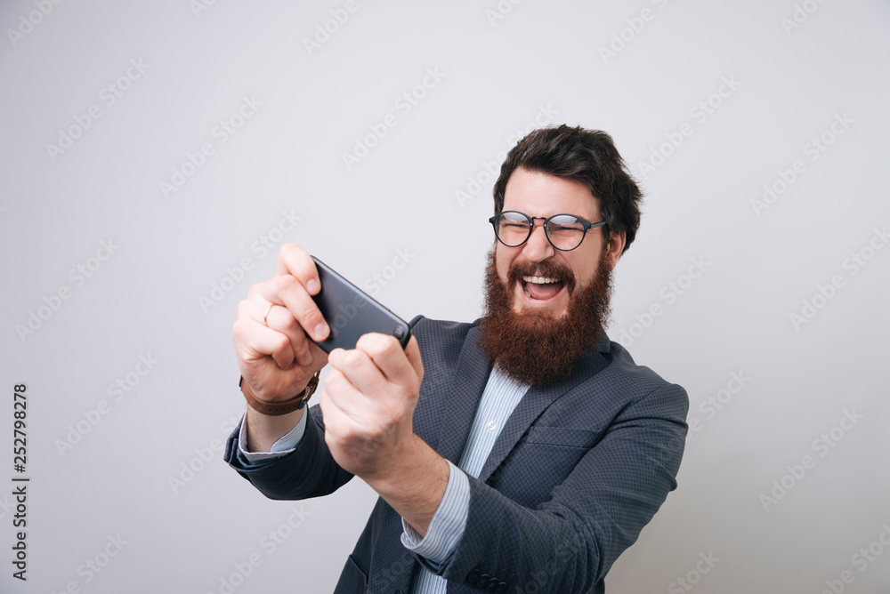 Businessman is actively playing games on phone on light gray background Businessman is actively playing games on phone on light gray background
