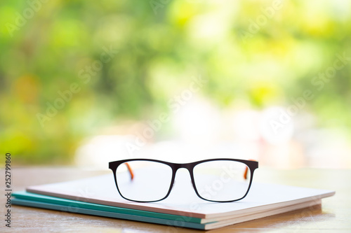 Black eyeglasses with three white notebook on wooden table, Bokeh garden background, Close up & Macro shot, Selective focus, Stationery concept