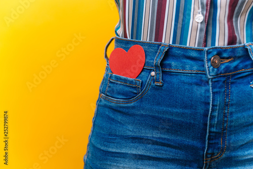 Close up on female wearing jeans with red heart in her pocket over yellow background photo