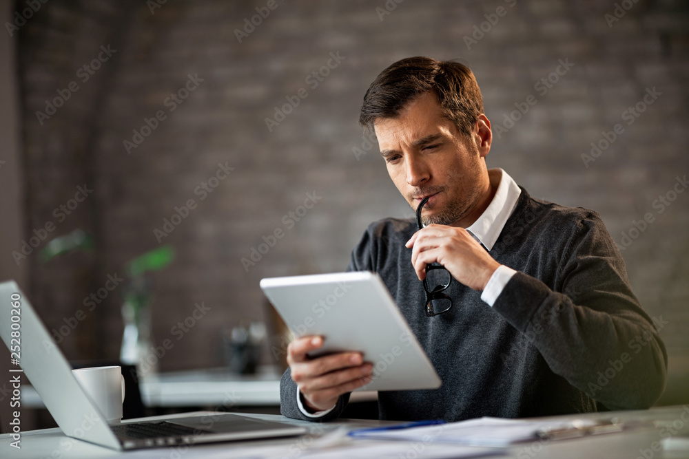 Pensive businessman reading something on digital tablet at work. Pensive businessman reading something on digital tablet at work.