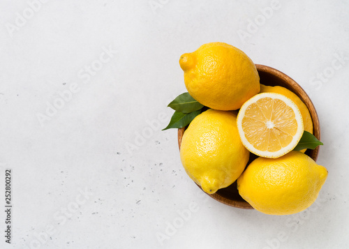 Ripe lemons in bowl with leaves on white background