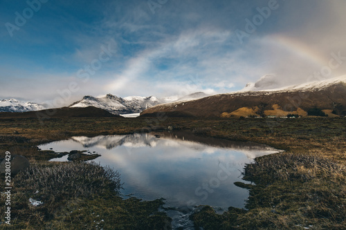 Idylic Icelandic nature with lake, blue sky, rainbow and snowy glacier in the background 